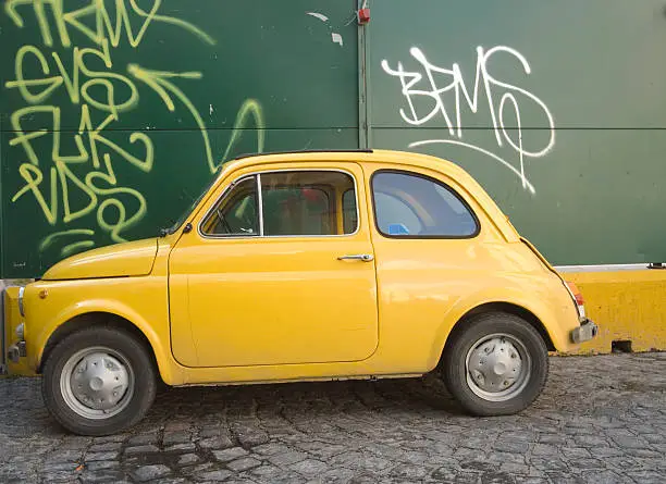 Vintage Italian car: Fiat 500, yellow color on green and yellow wall.