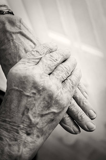 istock Old woman's hands, folded, retirement home window, sepia toned 157563953
