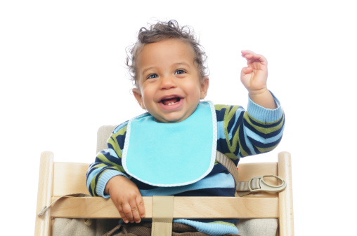 A biracial baby shows his excitement while sitting his highchair awaiting a meal