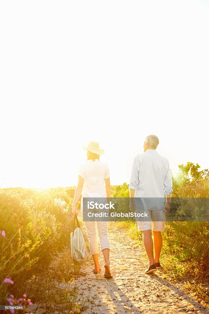 Casal andando em uma estrada de terra durante o pôr-do-sol - Foto de stock de 50 Anos royalty-free
