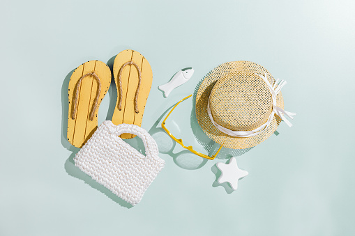 Summer flat lay with beach accessories, sunglasses, sunhat, beach shoes, white bag. top view on mint background, copyspace. Summer holiday or vacation concept, sunlight shadow, aesthetic minimal photo