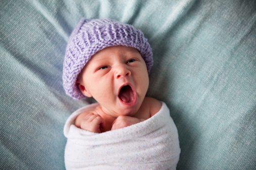 Color photo of a newborn baby yawning while wrapped in a blanket.