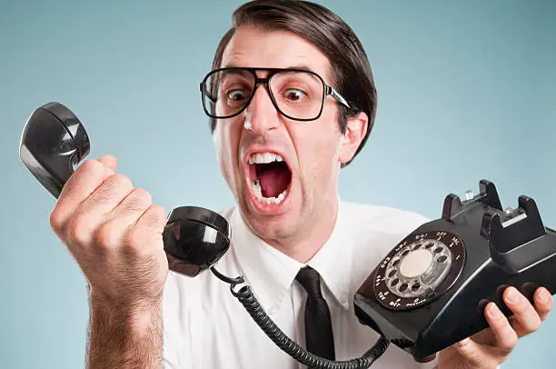 Nerdy office worker in short sleeved shirt, with attitude, holding a black rotary vintage phone.