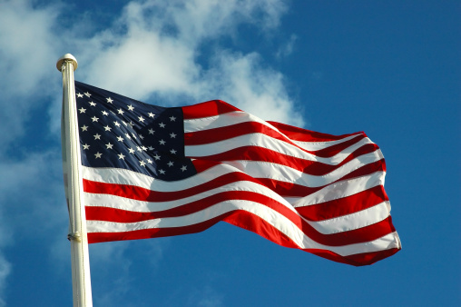 The American Flag flying in the wind in blue skies without clouds.  There is a fold in the flag showing the action of the wind.