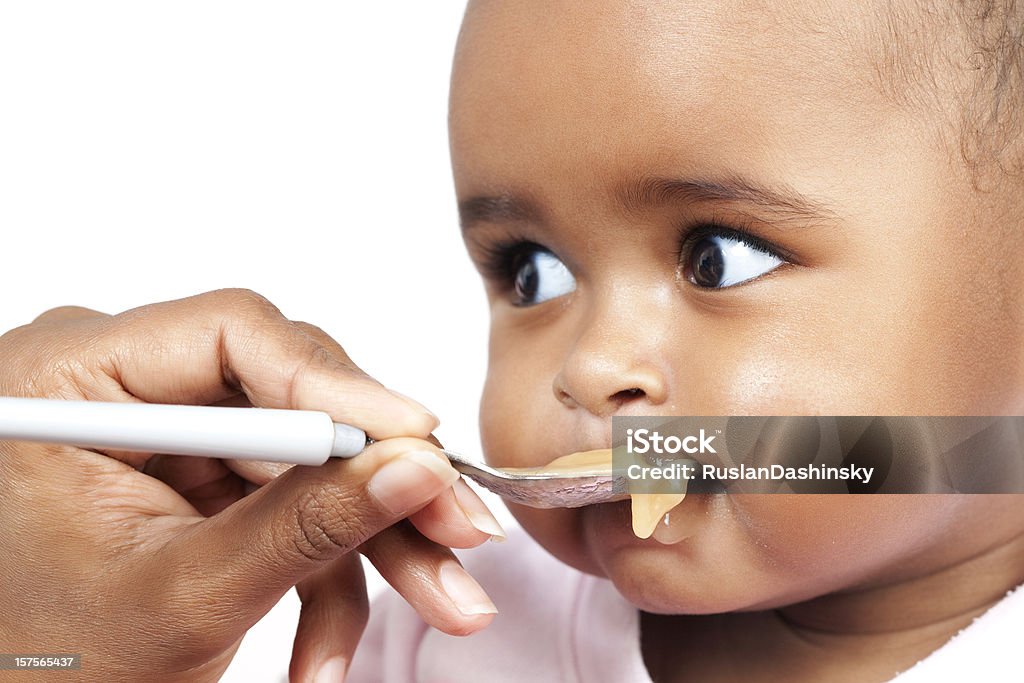 A baby being fed baby food on a white spoon 5 month old daby is being fed by her mum. Baby - Human Age Stock Photo
