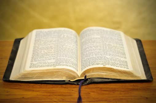 Old dusty well-used bible on timber table with golden background