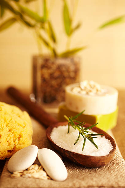 Spa still life of Rosemary on bath salt scrub in wooden spoon on linen, with bath sponge, bars of soap, bamboo, close-up