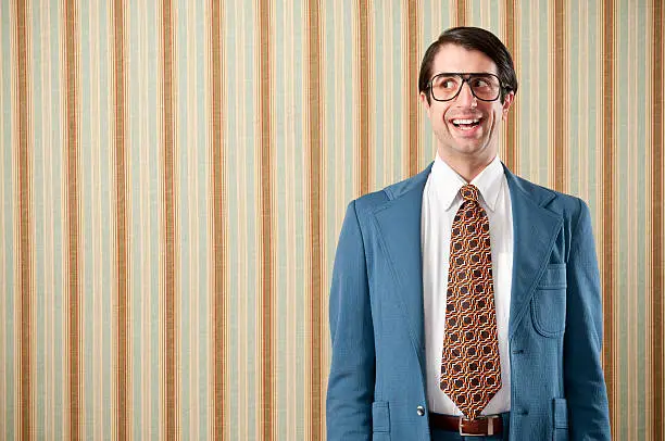 Nerdy businessman wearing a blue retro suit giving a thumbs up. The wall has a striped wallpaper..