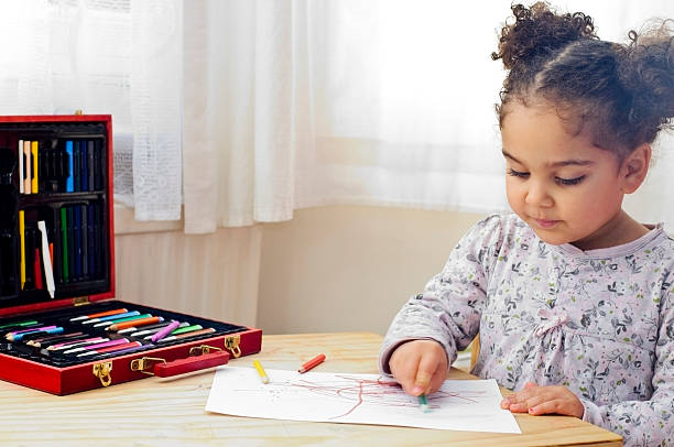 Child with pony tails drawing with colored crayons