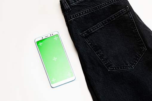 Flat Lay Shopping with smartphone, chroma key green screen, jeans cloth on white background. E-commerce, applications, online purchase. Modern technology. Horizontal Plane. Denim.