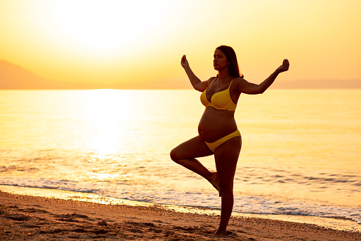 Photo of a pregnant woman doing yoga at the seaside in sunrise
