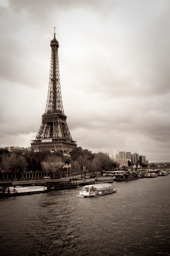View of the Eiffel Tower with some Bateaux-Mouches on the Seine, Paris. Desaturated effect, vintage look. Cloudy day on one of the most beautiful city in the world. Vertical shot with lots of details. Copy space.