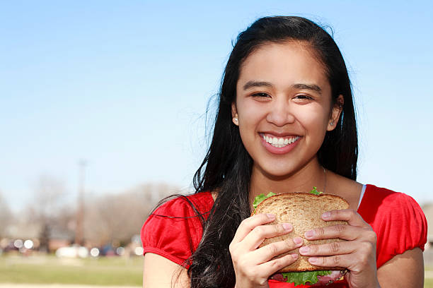 souriante jeune femme mangeant sandwich sur le parc - freedom sandwich bread food photos et images de collection