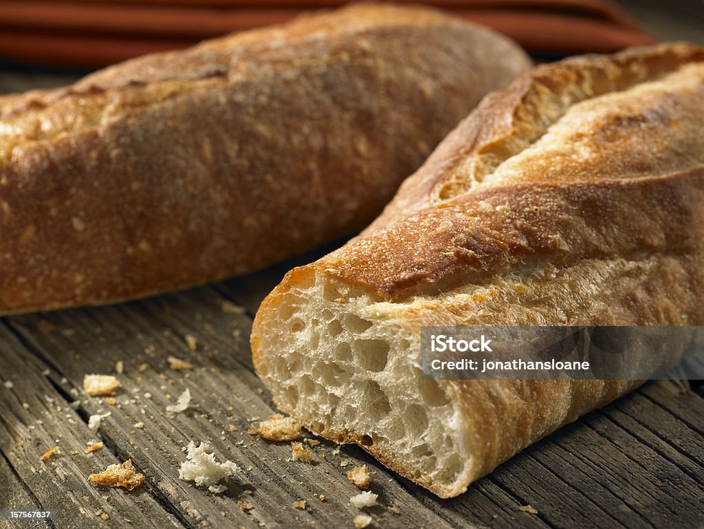 Baguettes with crumbs on weathered background Two fresh baguettes on a wood background. Selective focus is on the cut loaf. Baguette Stock Photo