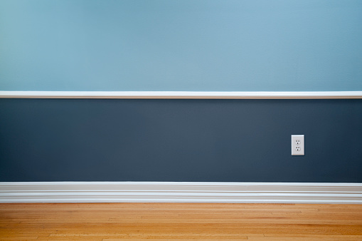 Empty room with wood flooring, blue wainscoting and a power outlet.