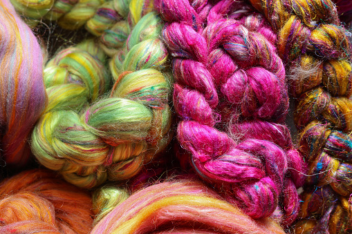 Closeup detail of colourful sheep wool merino, alpaca and silk fibres in a roving pleat, ready for spinning on traditional spinning wheel.