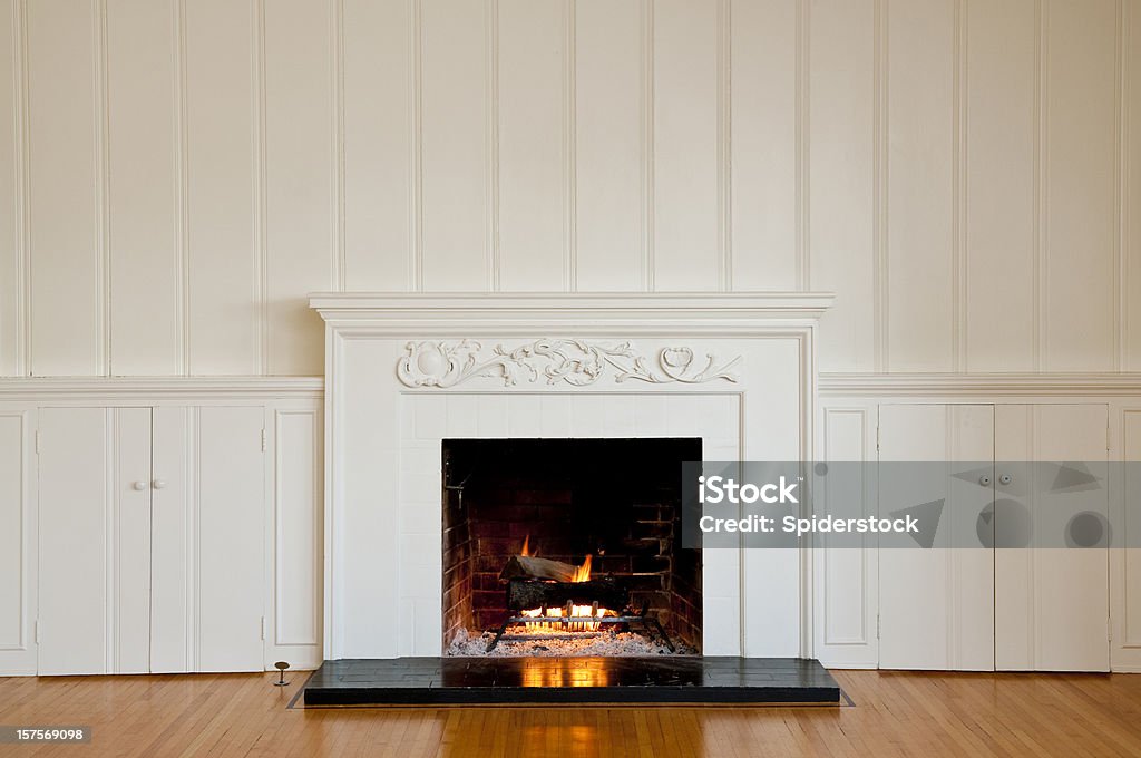 Traditonal Fireplace In Empty Room Traditional fireplace with floral relief moulding in empty domestic room.  There is a real roaring fire in the fireplace. Fireplace Stock Photo