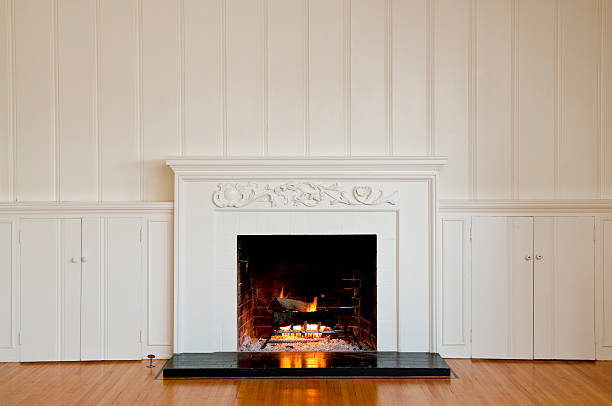 Traditonal Fireplace In Empty Room Traditional fireplace with floral relief moulding in empty domestic room.  There is a real roaring fire in the fireplace. wood paneling photos stock pictures, royalty-free photos & images