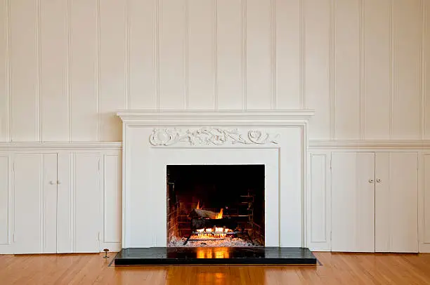 Traditional fireplace with floral relief moulding in empty domestic room.  There is a real roaring fire in the fireplace.