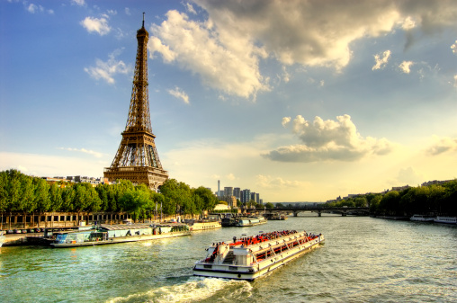 Eiffel tower and quay Seine river with barges and trees at sunset.