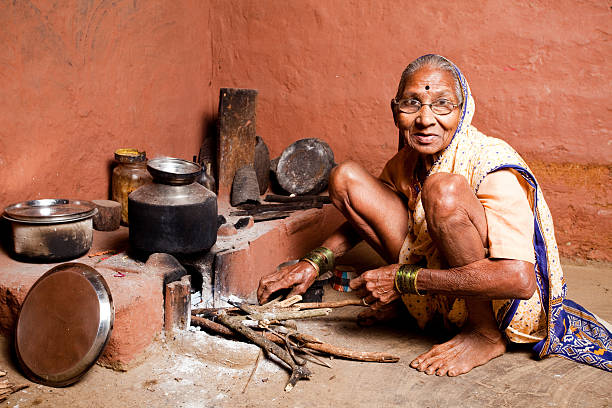 One Cheerful Rural Indian Senior Woman preparing food Cheerful Rural Indian Senior Woman preparing food in an old fashioned kitchen in Rural Indian Village. It's still a very common way of preparing food across the Indian Villages village maharashtra stock pictures, royalty-free photos & images