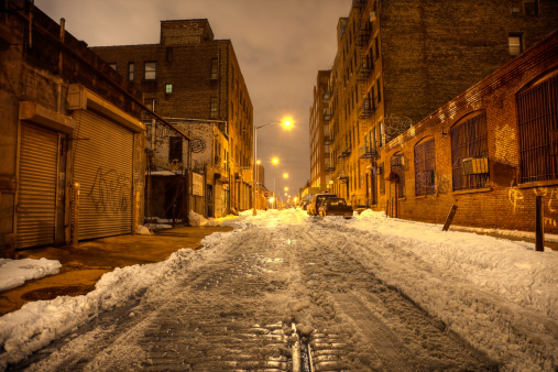 Dark city street in Brooklyn, New York. Photo taken after a snowstorm on a empty street the Dumbo neighborhood of the borough of Brooklyn. The snow  is partially melted on the old cobblestoned street lined with industrustrial warehouses.