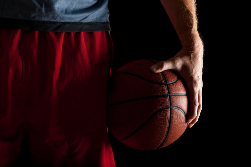 A hand holds a lit basketball on a black background, close-up, the start of the game, sports background