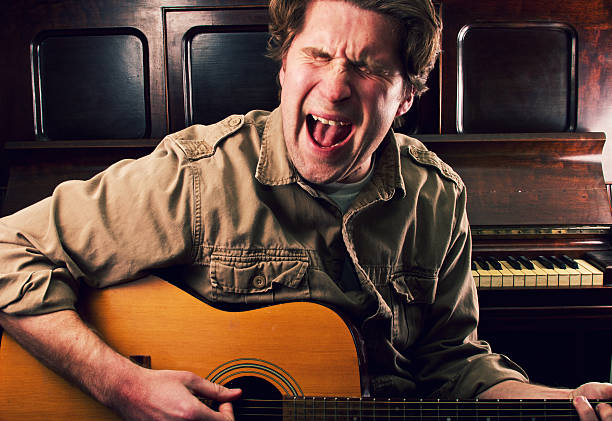 a male musician plays his guitar and sings in studio.