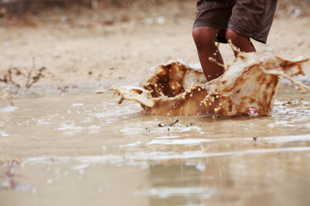 2 year old boy and 3 year old girl are enjoying and playing in a puddle of stranded rainwater.