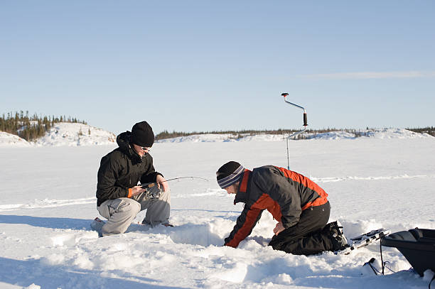 Ice Fishing, Yellowknife. A man and woman fish through a hole in the ice on Great Slave Lake in Canada's Arctic.  Click to view similar images. ice fishing stock pictures, royalty-free photos & images