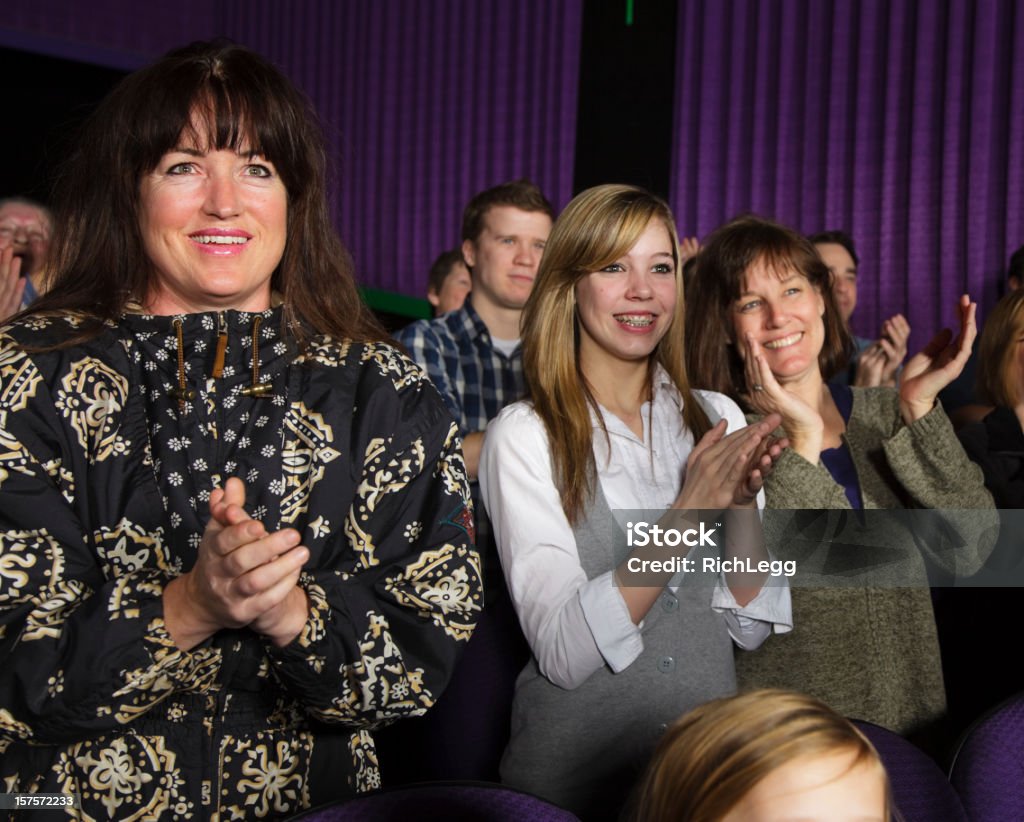 Happy Audience Members A happy young woman standing in a concert watching the performance. Applauding Stock Photo