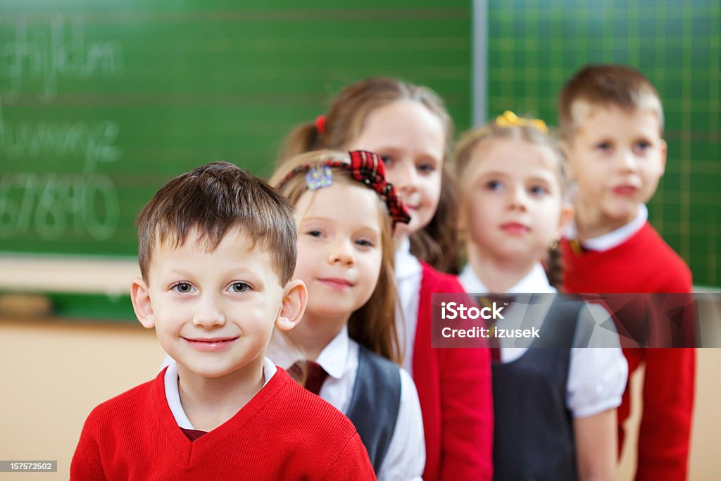 School Kids Standing In A Row, Classroom Elementary school kids in a classroom standing in a row and looking at camera. Focus on a boy in the foreground. Green Color Stock Photo
