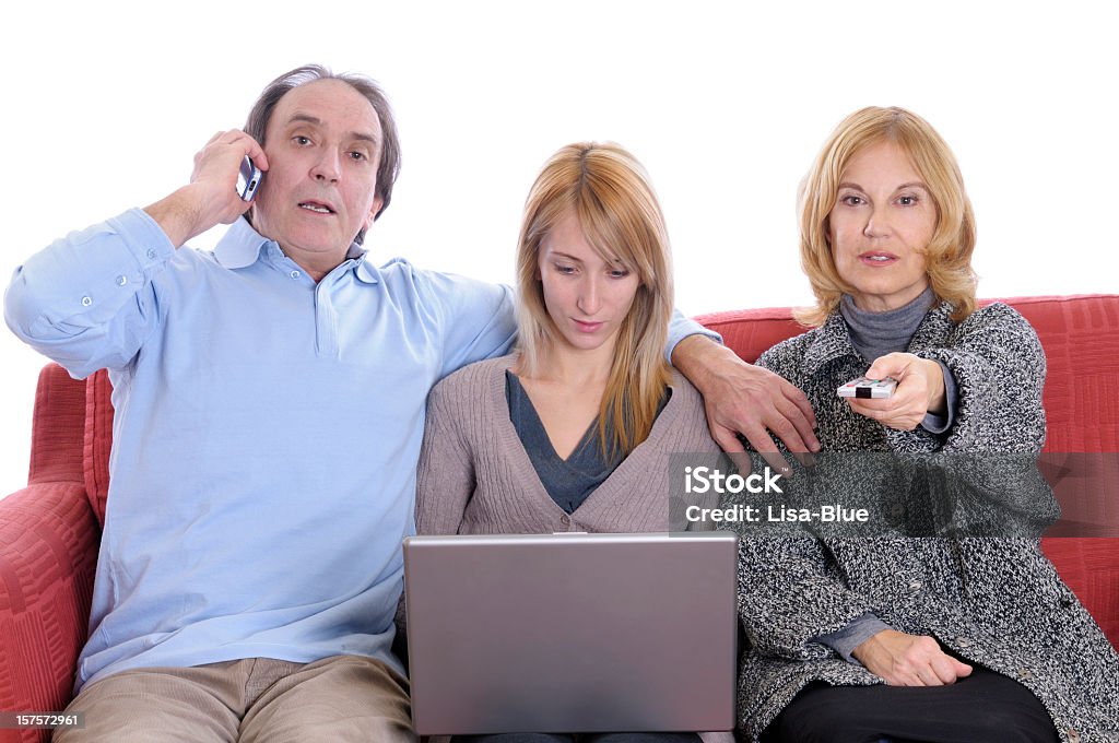 Busy Family on Red Sofà Father talking on the phone while daughter using pc and mother watching tv Family Stock Photo