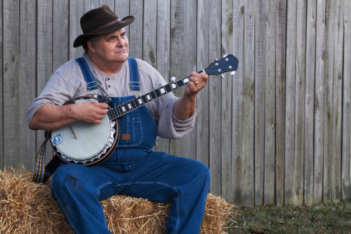 a bluegrass country banjo player sitting on a haystack at dusk. 