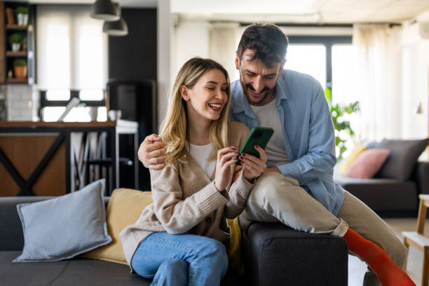 istock Smiling young couple embracing while looking at smartphone. Multiethnic couple sharing social media 1575731428