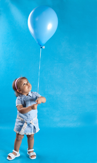A 20 month old toddler holding a balloon and looking up at it.