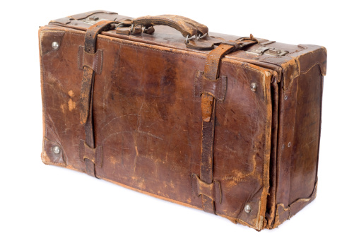 Old fashioned vintage brown leather suitcase with a film camera, a straw hat and two passports on white. Ready for travel and holiday concept