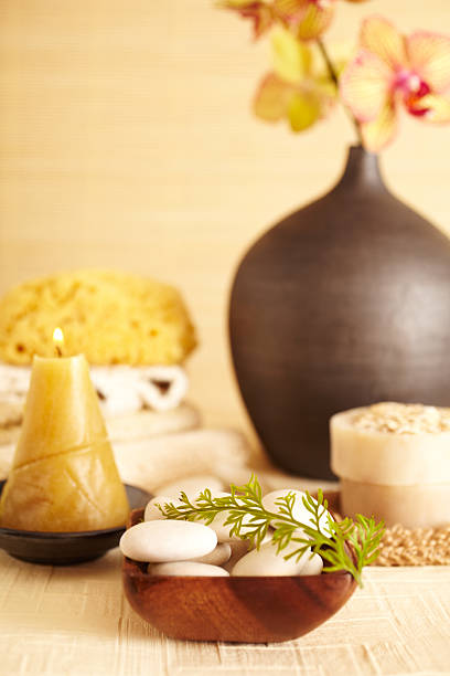 Spa still life of white rocks with fern leaf, candle, orchid flower in bathroom with towels, oatmeal soap, and bath sponge, close-up