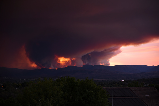 Bush fires burn the hills around a city. Heavy smoke clouds darken the sky