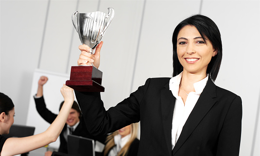 Young caucasian businesswoman holding a trophy in a meeting with her team