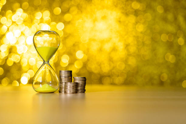 Hourglass and coins on shiny golden background.