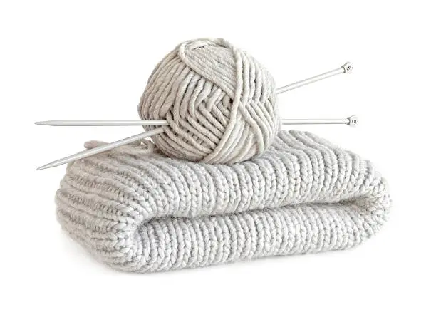 Hand-knitted work of a very thick gray wool yarn with two knitting-needles of size six stuck through the skein isolated on white background.