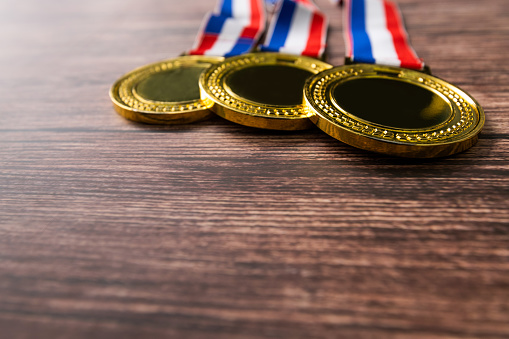 Three gold medals on wooden table.