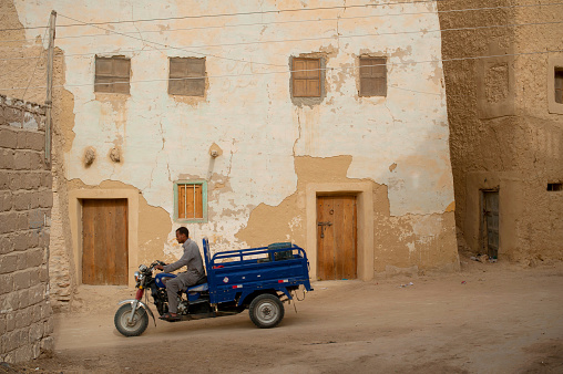 Siwa, Egypt, April 11th 2018\nMotorcycle pick-up being driven through the mud brick houses of Siwa Oasis, Egypt.