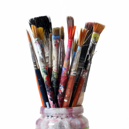 A few paintbrushes in a glass container on white.