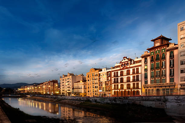View of the old town of Malaga city and the Guadalmedina river from the left riverside with the evening sunlight, and some birds flying. (South of Spain, Europe)