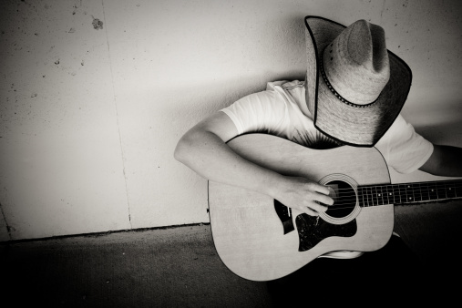Cowboy playing the guitar. Black and white image with contrast added.