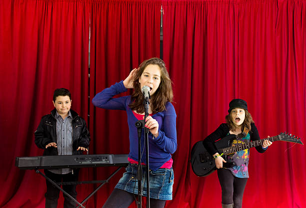 Three children, aged from eight to thirteen playing music on stage.