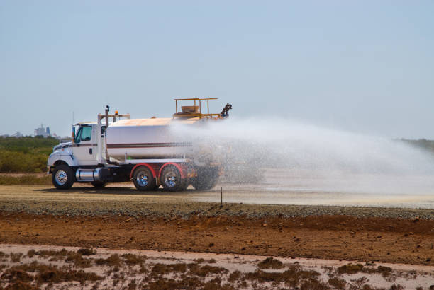 Water tank truck spraying water on a new road construction site in preparation for paving.