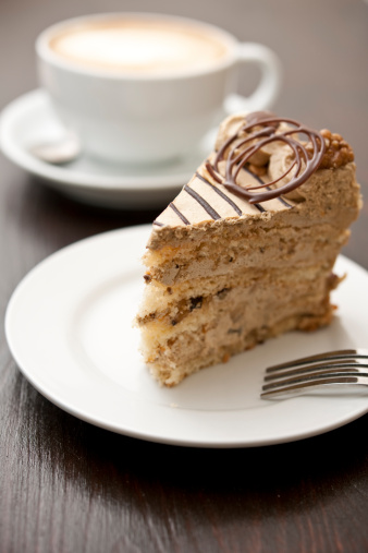 Slice of Coffee and walnut cake with an out of focus latte-cappuccino in the background.